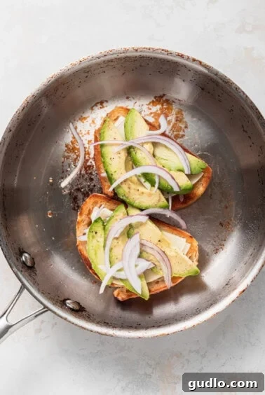 Avocado and red onion layered on cheese and bread in a pan.