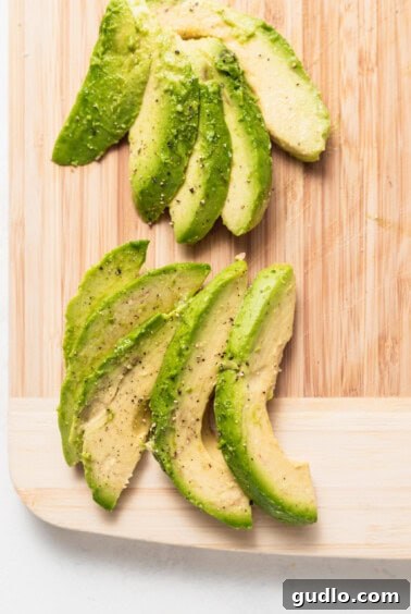 Avocado slices beautifully fanned out on a cutting board, seasoned with salt and pepper.