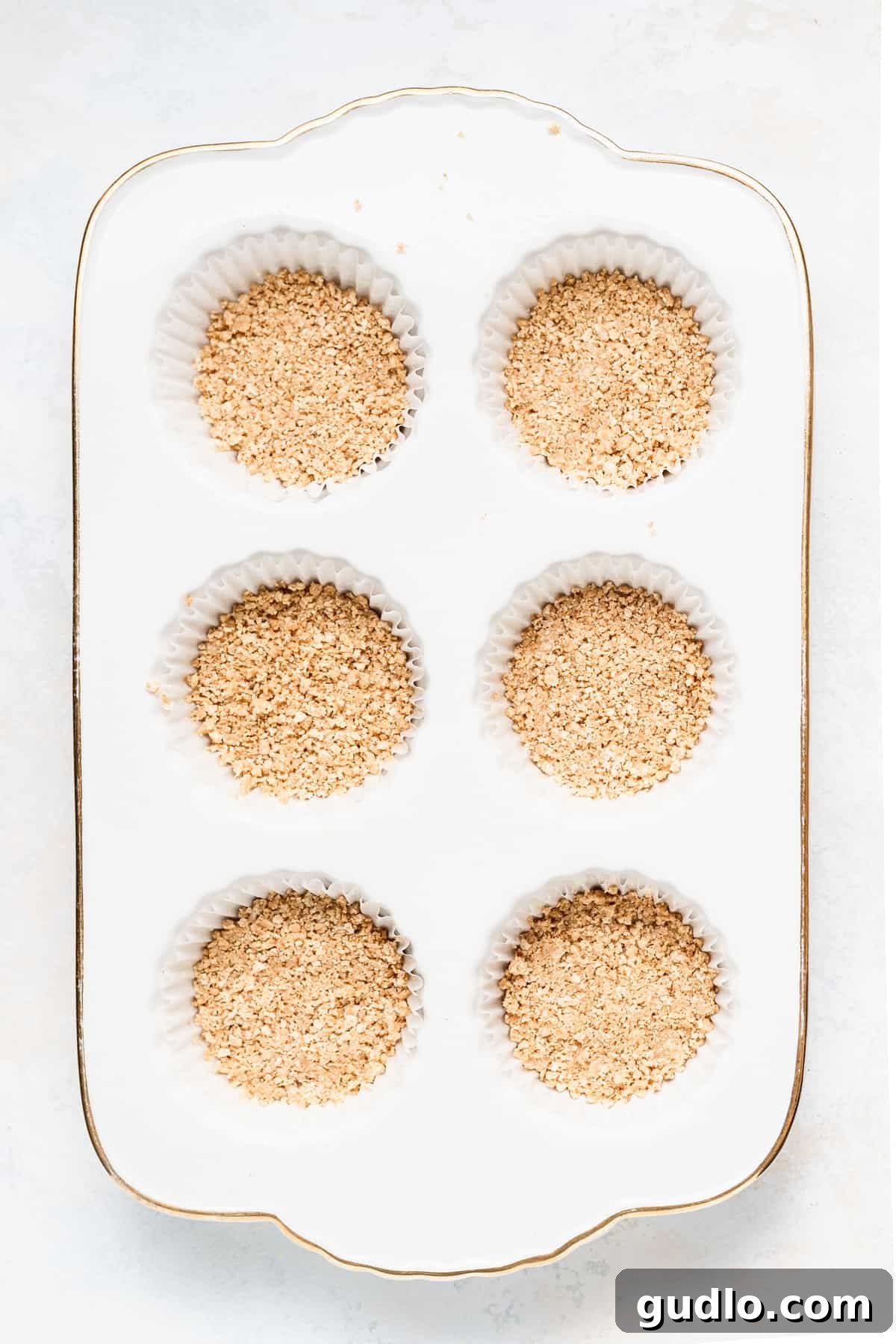 Bite-Sized Cheesecake Delights 3 Close-up of a perfectly pressed graham cracker crust inside a muffin liner, ready for filling.