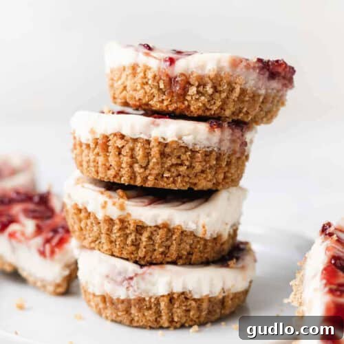 A stack of lemon raspberry cheesecake bites on a white plate, garnished with fresh raspberries.