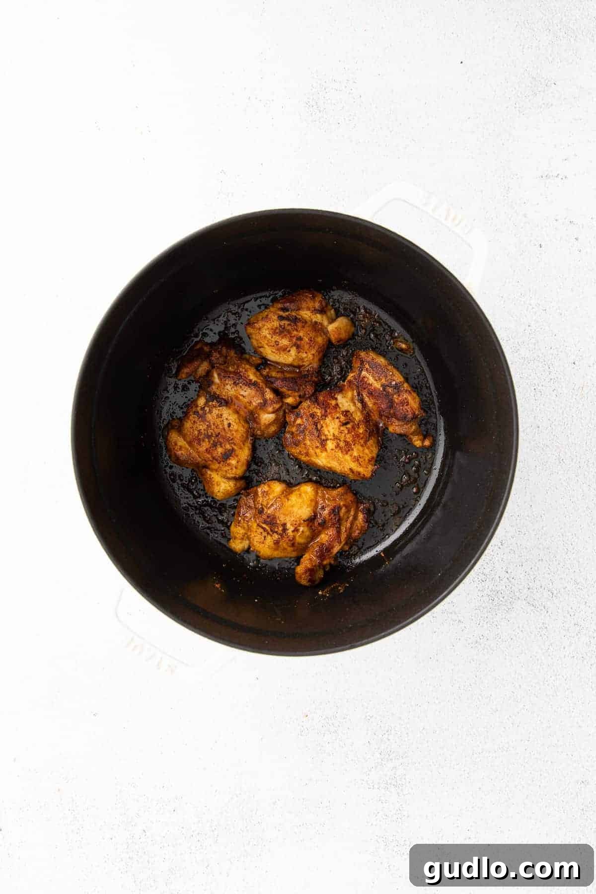 Seared chicken thighs cooking in a black pan, achieving a beautiful golden-brown crust.