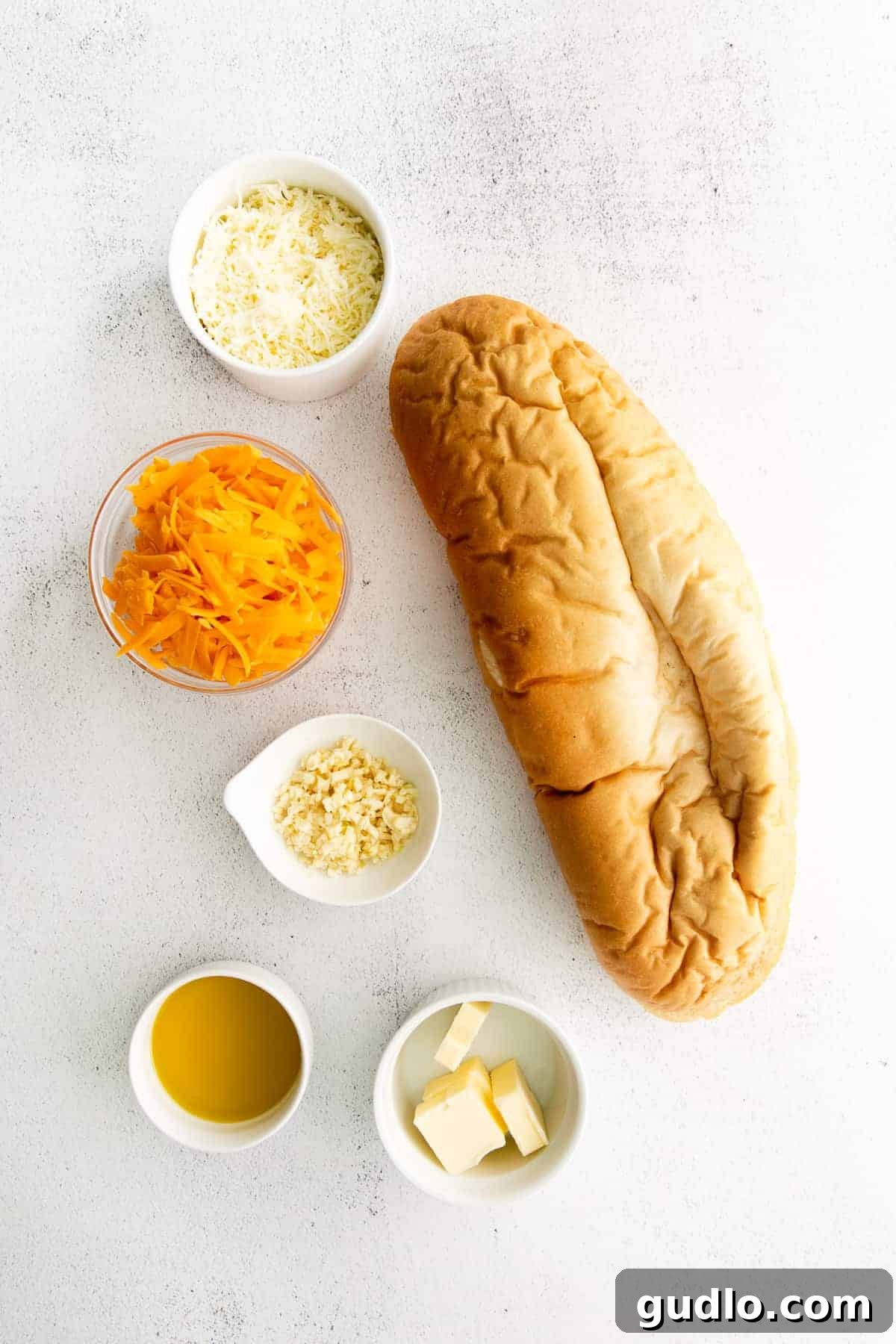 Golden Cheesy Garlic Bliss 4 All the ingredients for cheesy garlic bread laid out on a kitchen counter: Italian bread, butter, olive oil, garlic, cheddar cheese, and mozzarella cheese.