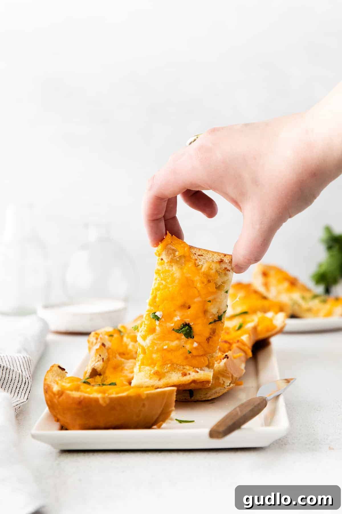 Golden Cheesy Garlic Bliss 10 A hand reaching for a slice of cheesy garlic bread on a wooden board.
