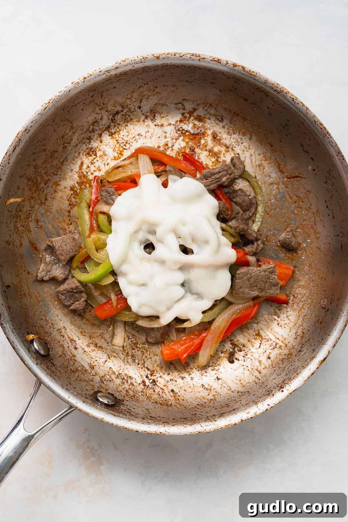 Philadelphia's Signature Sandwich 4 Melted provolone cheese draped over a steaming pile of sautéed peppers, onions, and steak in a pan.