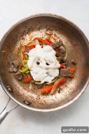 A frying pan showing a mix of meat, peppers, onions, and melted cheese.