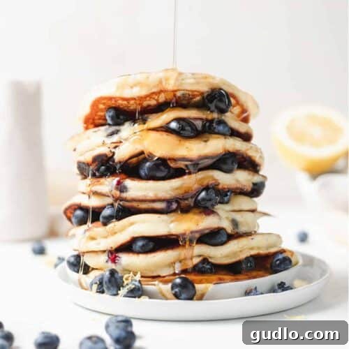 Beautifully stacked ricotta pancakes on a plate with blueberries and syrup