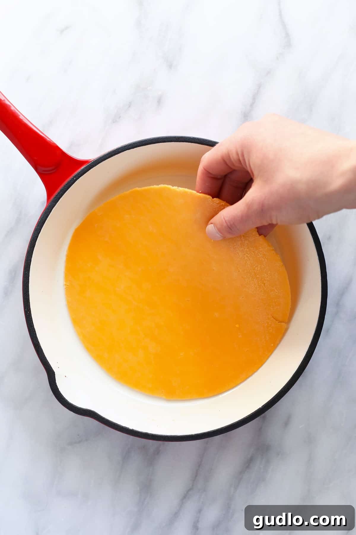 Placing a piece of cheese in a small skillet for cooking.