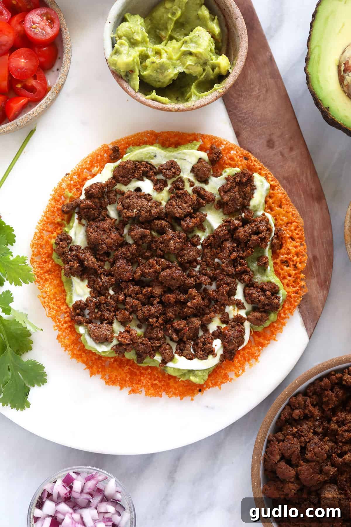 Close-up shot of a cheese tortilla being filled with fresh guacamole, creamy Greek yogurt, and seasoned ground beef, preparing for assembly.