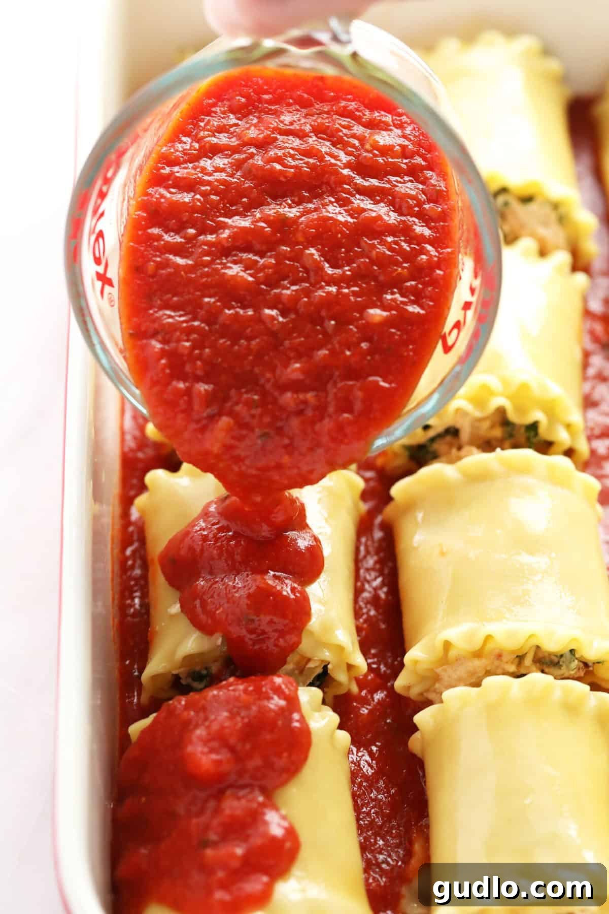 Wholesome Kale Lasagna Roll Ups 5 Rich marinara sauce being poured generously over assembled Kale Lasagna Roll Ups in a baking dish.