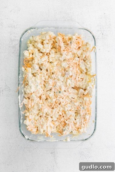Crispy Golden Cheese Potatoes 4 An uncooked cheesy casserole dish with shredded carrots, ready for the oven.