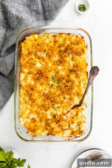 Crispy Golden Cheese Potatoes 5 Cheesy hashbrown potato casserole served in a glass dish with a fork, ready to eat.