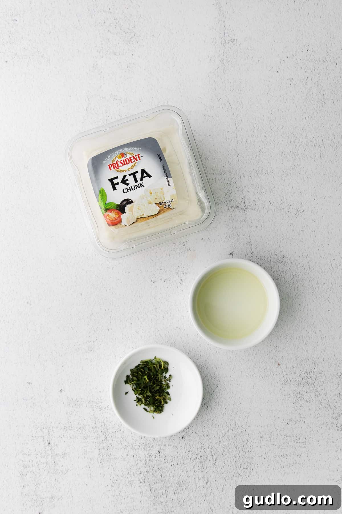 Flame-Kissed Feta 3 A beautifully composed shot featuring a block of fresh feta cheese, a bottle of olive oil, and sprigs of fresh thyme laid out on a kitchen countertop, highlighting the simplicity of the ingredients for the grilled feta recipe.
