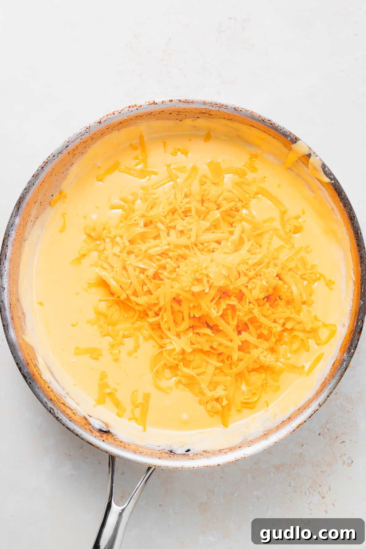 shredded cheese melting in a skillet for pretzel cheese dip Close-up shot of freshly shredded cheddar cheese slowly melting into a creamy sauce in a skillet, showing its smooth texture.