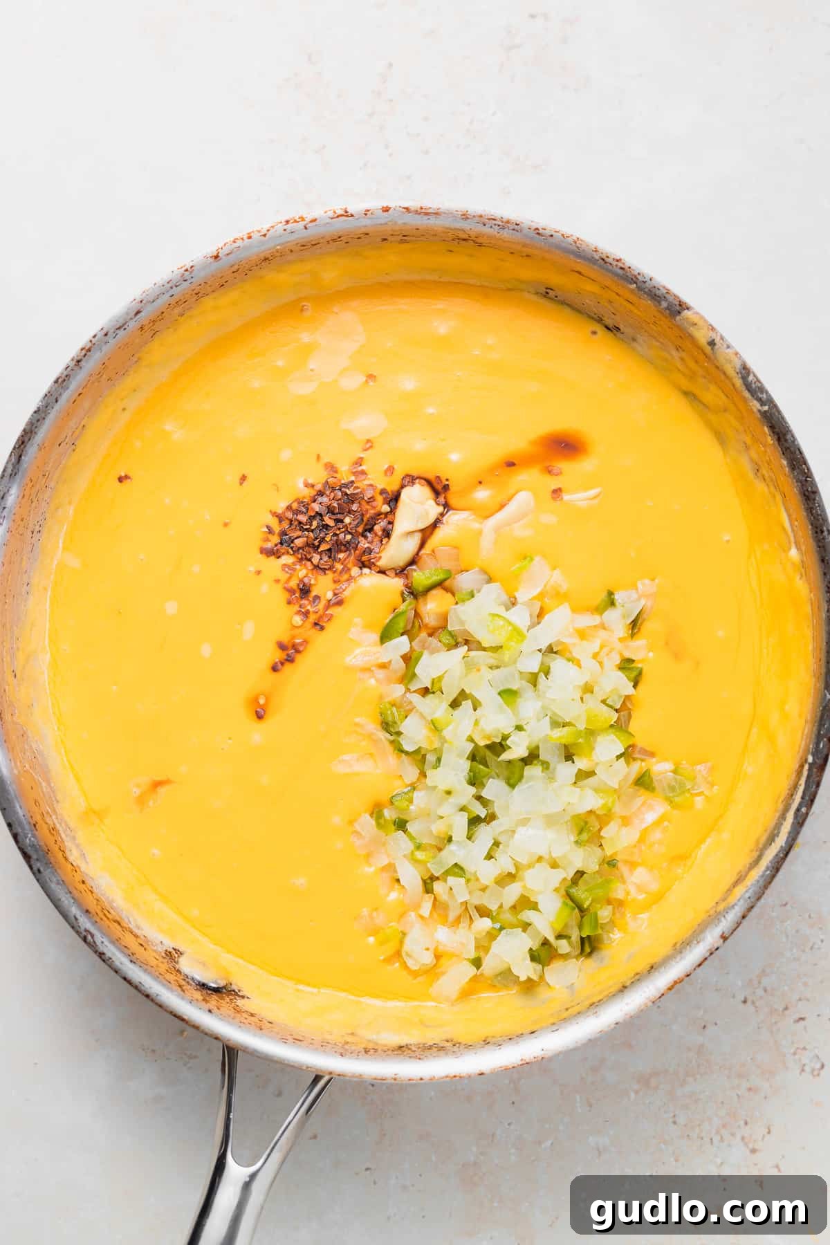 spices and onions and peppers being added to melted cheese sauce for pretzel cheese dip A frying pan filled with creamy pretzel cheese dip, featuring visible pieces of sautéed onions and peppers, awaiting its final stir.