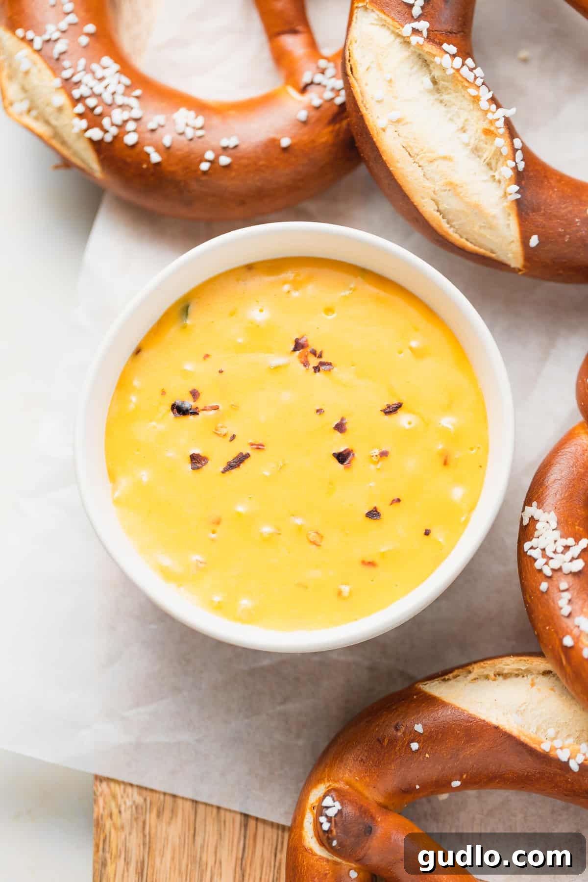 pretzel cheese dip in a bowl served next to soft pretzels A close-up of a rustic bowl filled with golden, bubbling pretzel cheese dip, served alongside a basket of warm, twisted soft pretzels.