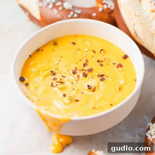 Melty Golden Pretzel Cheese Dip 2 A delicious bowl of pretzel cheese dip with soft pretzels, buns, and soup in the background.