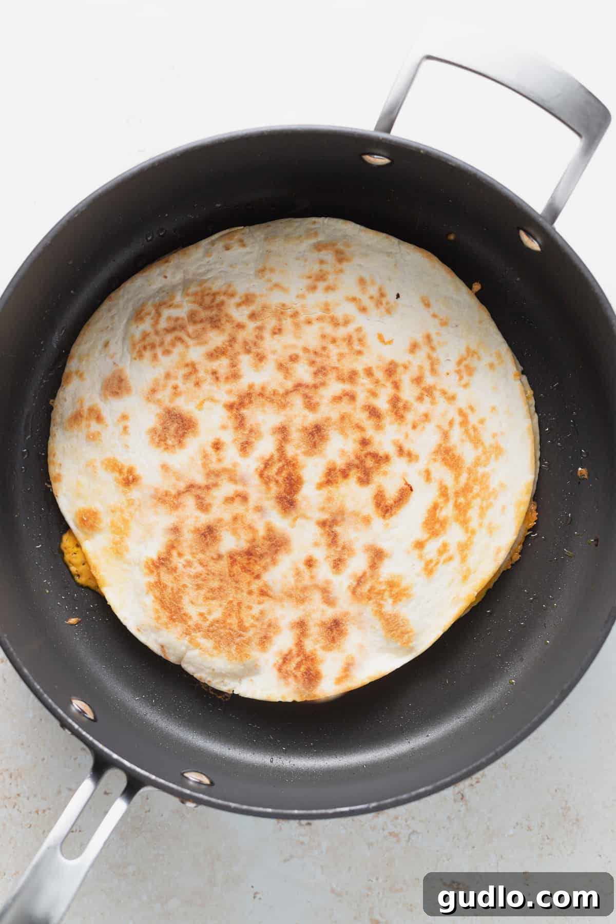 Quesadilla Browning in a Frying Pan A golden-brown cheese quesadilla cooking in a hot non-stick frying pan, cheese perfectly melted.