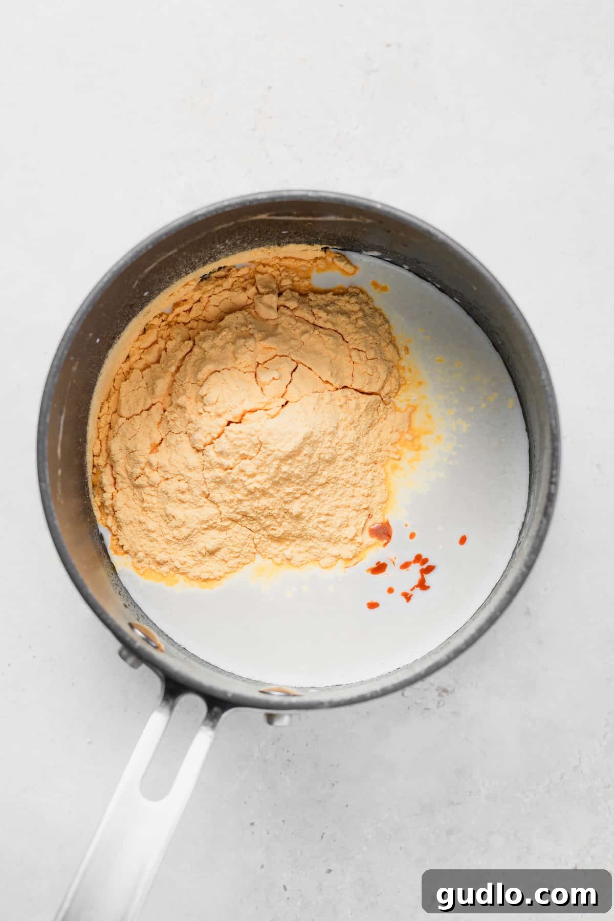 Mixing the creamy cheese sauce base for your mac and cheese cups. Powdered cheese mix and milk being stirred in a pot, ready for the macaroni.