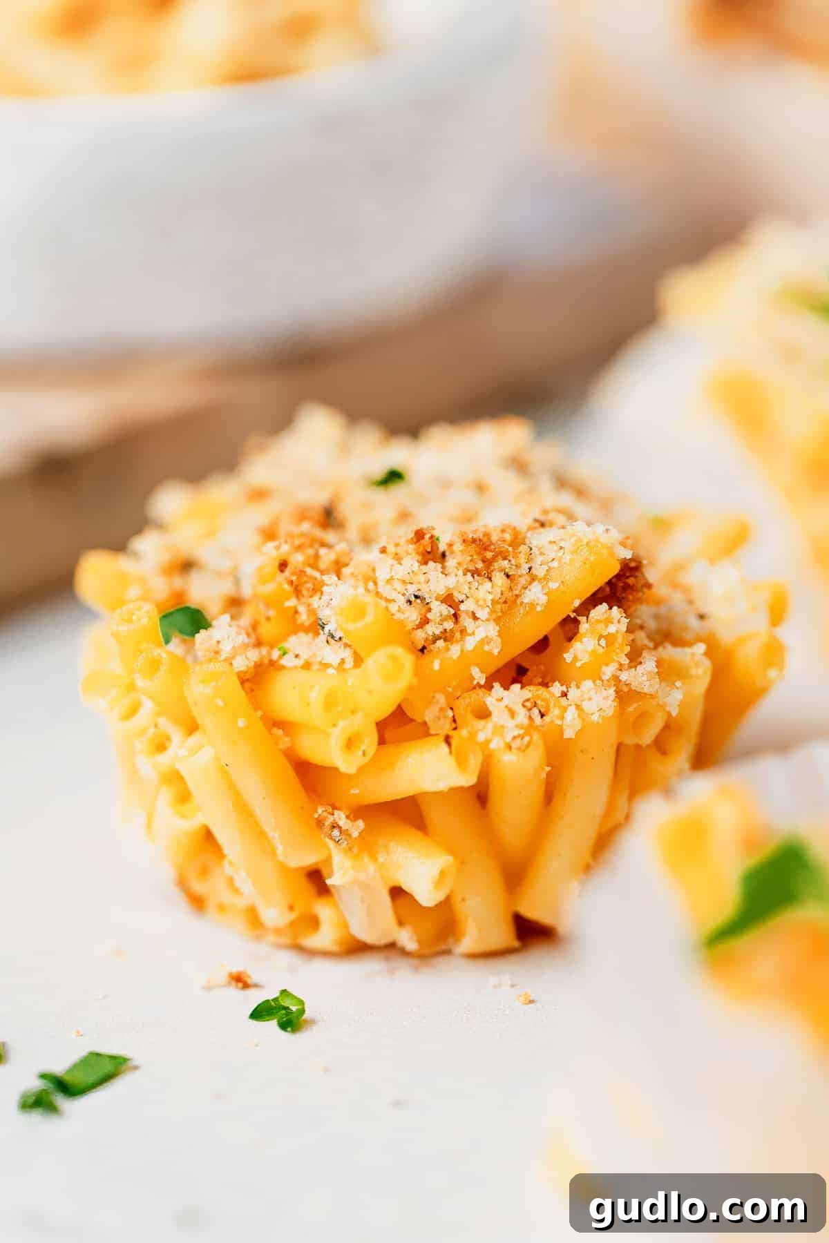 A perfectly baked mac and cheese cup, topped with crispy breadcrumbs and fresh parsley, ready to eat. Close-up of a single mac and cheese cup with golden breadcrumbs, garnished with fresh parsley.