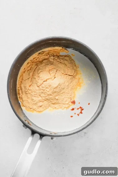 A frying pan containing the creamy cheese sauce with spices and powdered cheese mix.