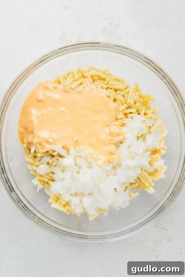 A glass bowl filled with macaroni noodles coated in cheese sauce and mixed with onions.