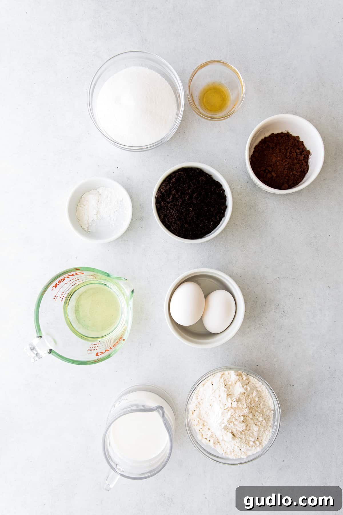 A selection of baking ingredients, including flour, sugar, eggs, and cocoa powder, neatly arranged on a kitchen countertop.