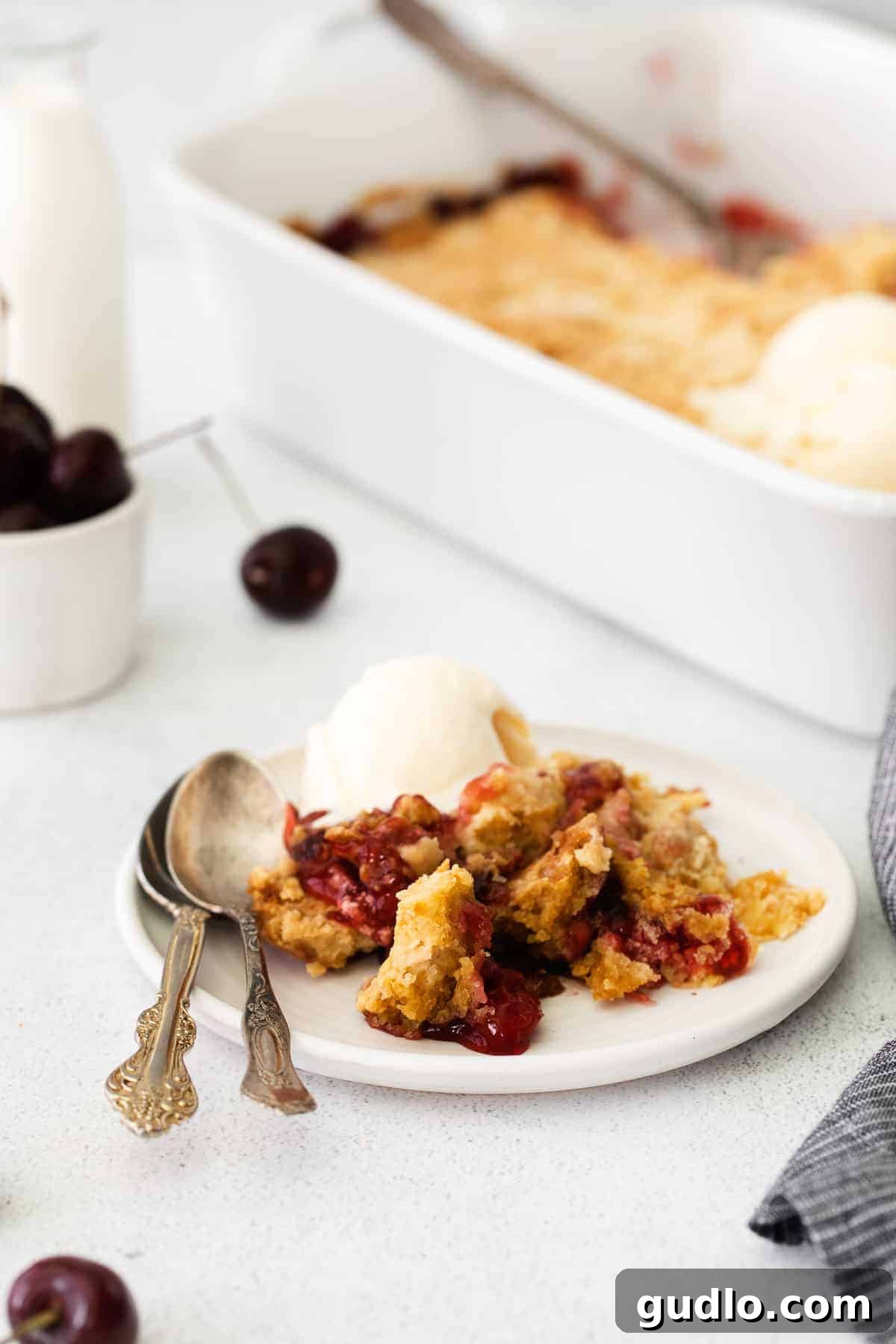 This Cream Cheese Cherry Dump Cake is calling your name! Dump all the ingredients into a cake pan, bake it, and enjoy topped with a scoop of vanilla ice cream. A slice of cherry dump cake on a white plate, ready to be enjoyed.