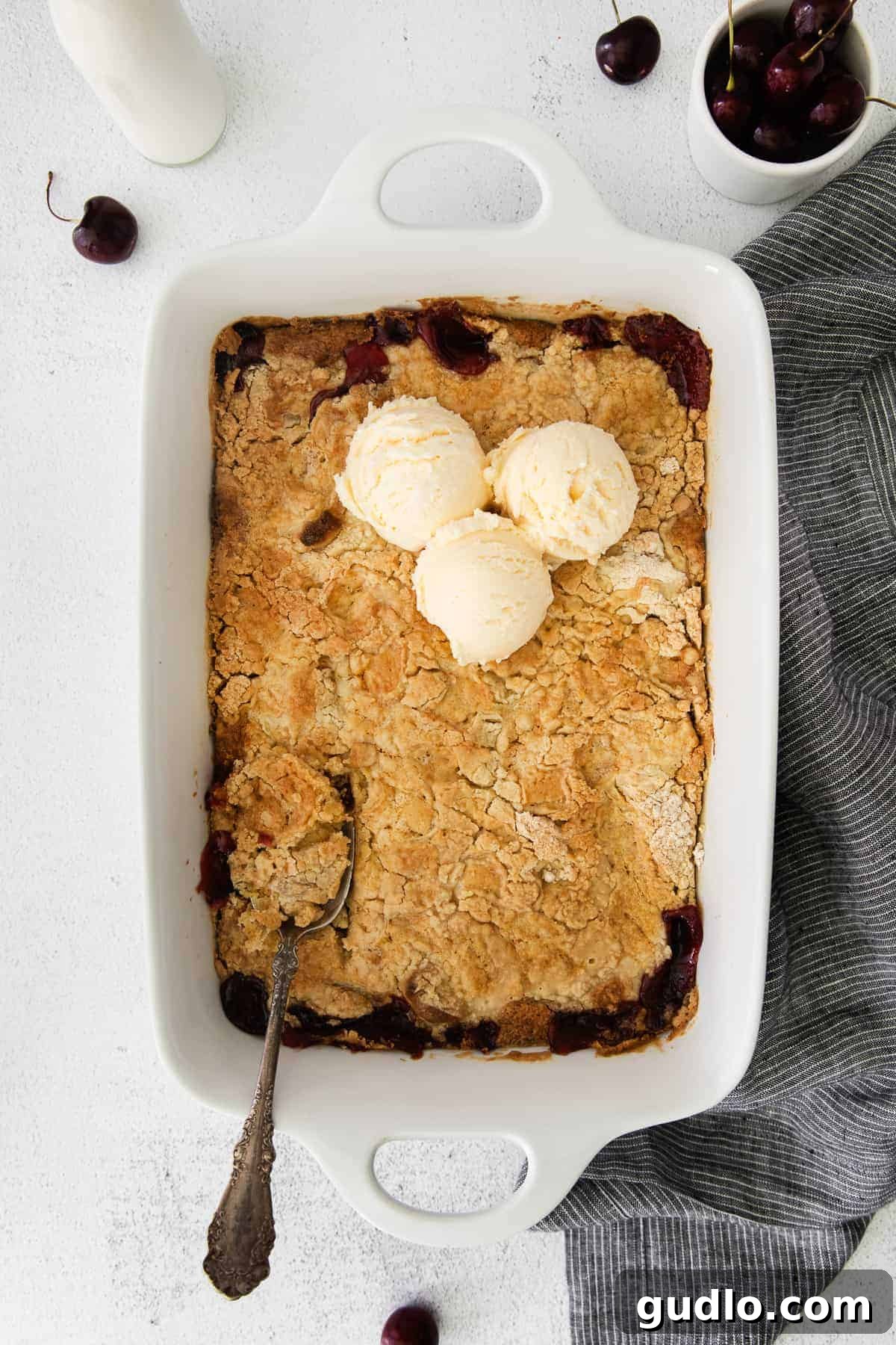 This Cream Cheese Cherry Dump Cake is calling your name! Dump all the ingredients into a cake pan, bake it, and enjoy topped with a scoop of vanilla ice cream. A baked cream cheese cherry dump cake in a casserole dish, fresh out of the oven.