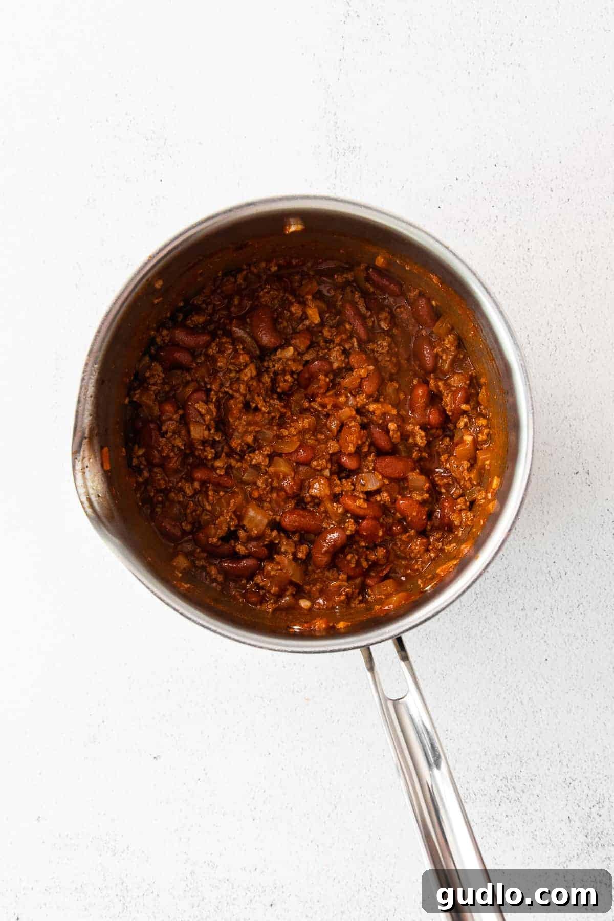 A pot of rich, simmering homemade chili, ready to top hot dogs.