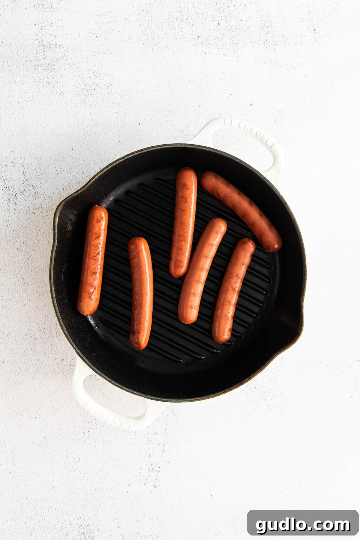 Seared hot dogs cooking in a pan, achieving a perfect golden-brown exterior.