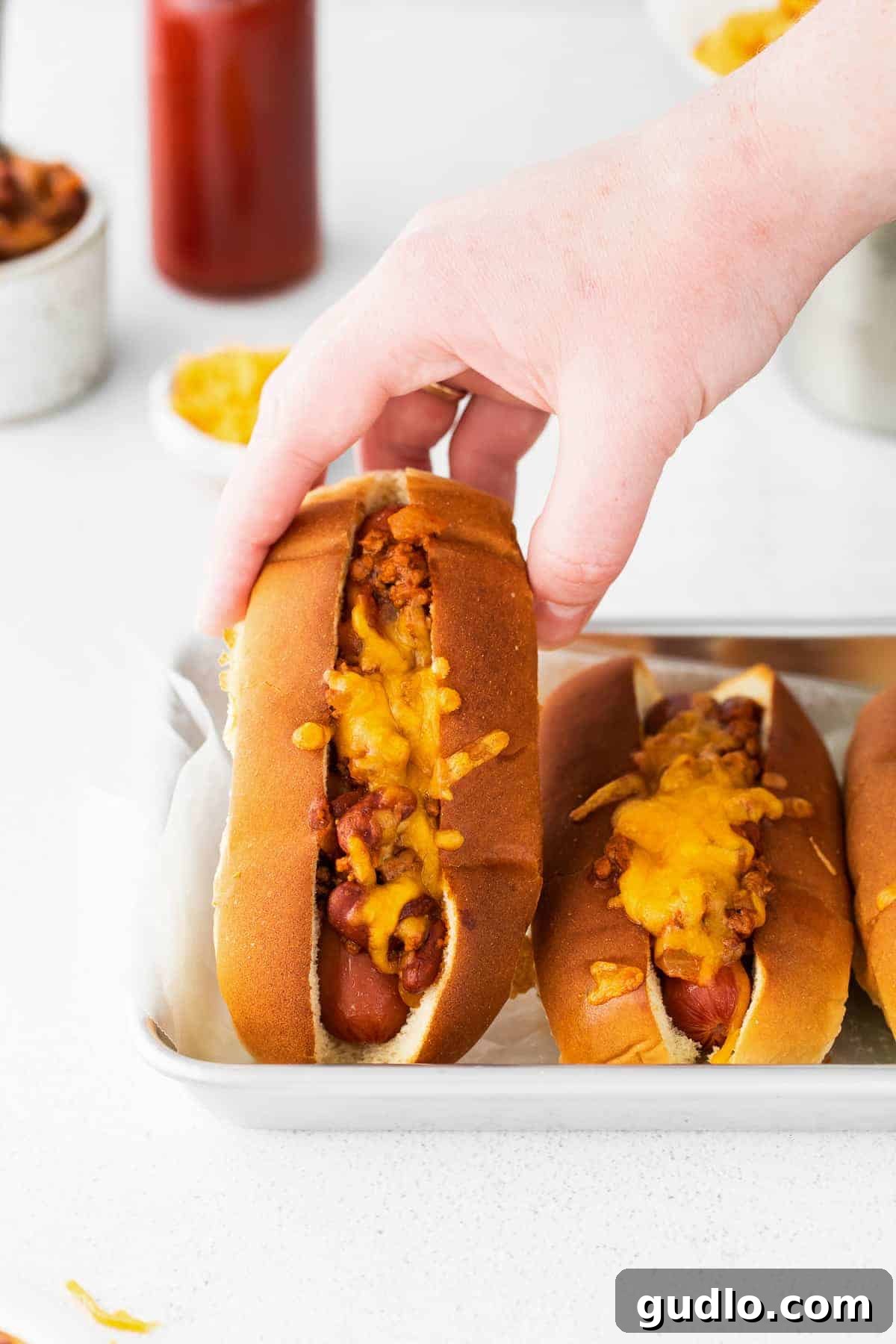 A hand holding a perfectly prepared chili cheese dog, showcasing the melted cheese and rich chili.