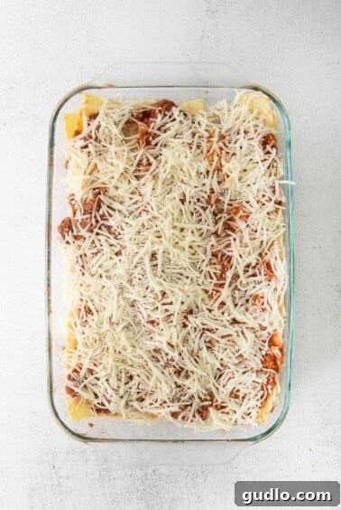 A casserole dish filled with layered lasagna, topped with meat sauce and a generous amount of shredded mozzarella cheese, ready for baking.
