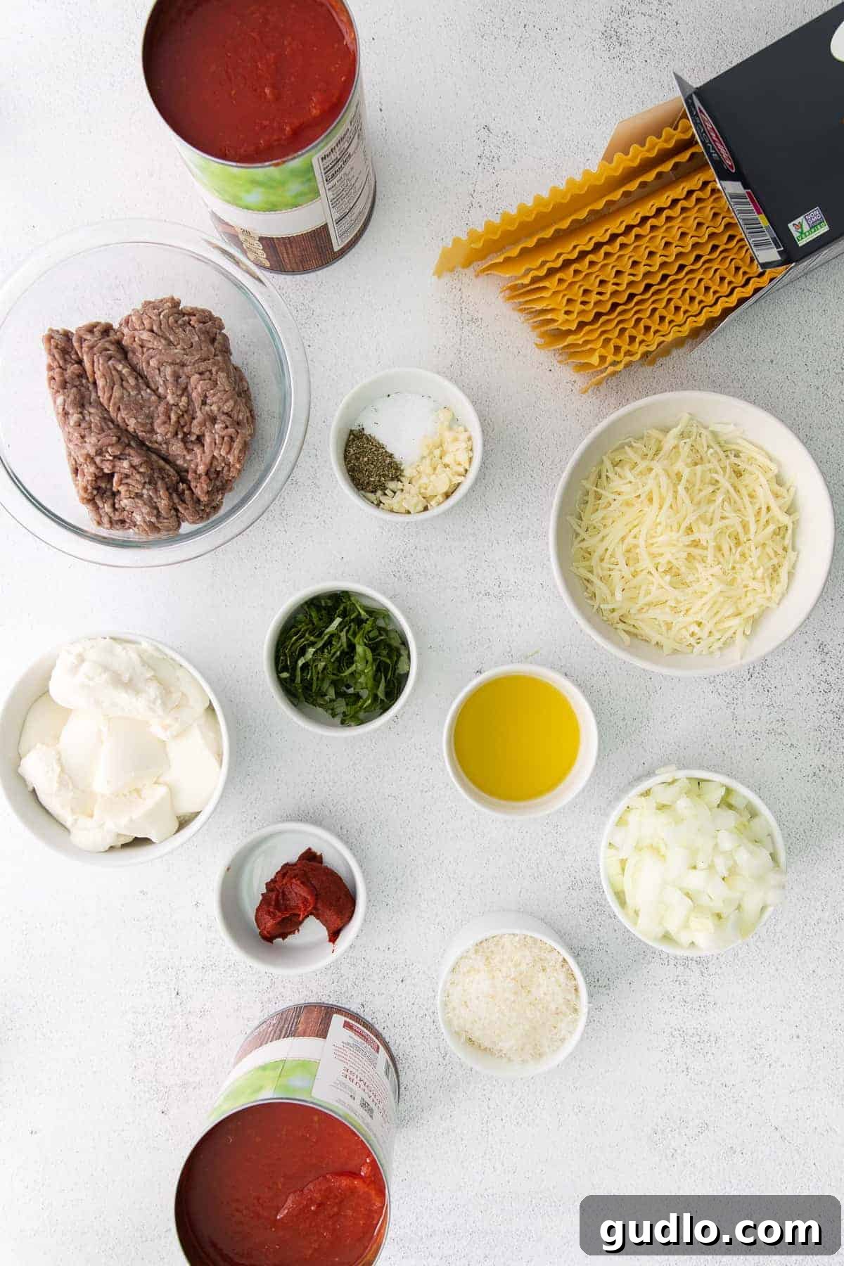 The Ultimate Meat Lasagna 3 All the fresh ingredients for homemade meat lasagna laid out on a kitchen countertop, including ground beef, tomatoes, onions, garlic, cheeses, and lasagna noodles.