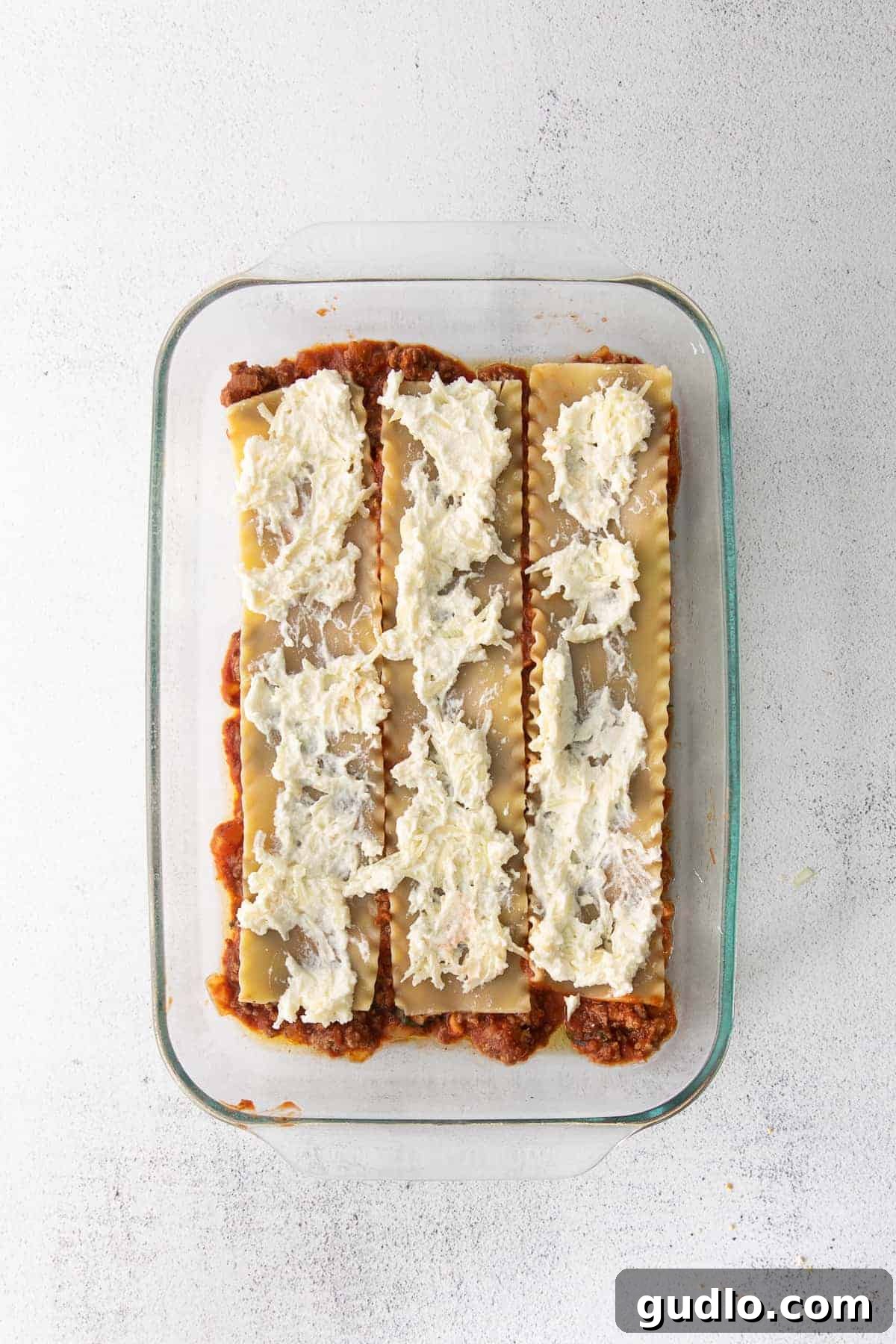 The Ultimate Meat Lasagna 5 Lasagna noodles covered with a creamy ricotta cheese spread in a glass baking dish, forming one of the delicious layers.