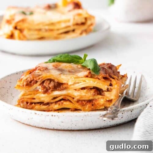 A perfectly baked meat lasagna on a plate, garnished with fresh basil, showcasing its rich layers.