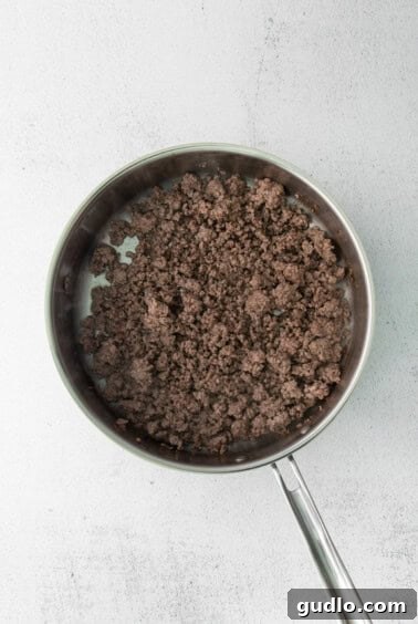 A frying pan filled with browned ground beef, ready for the next step in making the meat sauce.