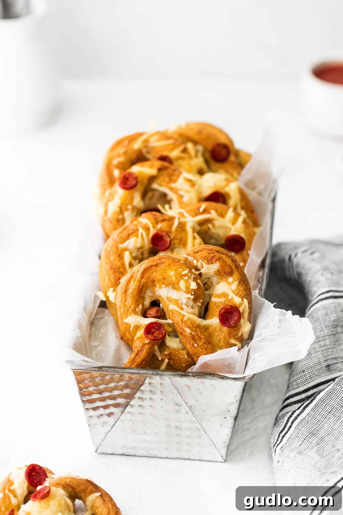 Pizza soft pretzels are such a fun snack or appetizer to make. They're made with a classic soft pretzel base and topped with pizza toppings! Delicious homemade pizza soft pretzels in a rustic tin, ready to be enjoyed as a family snack or appetizer.