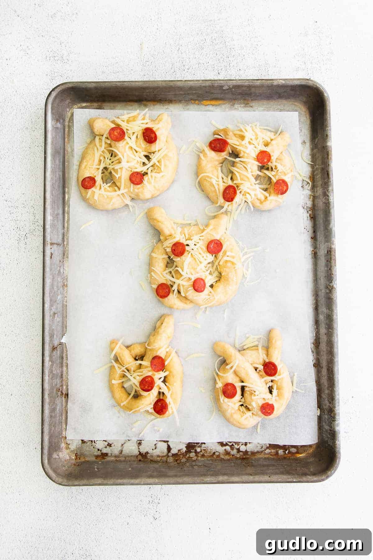 Pizza soft pretzels are such a fun snack or appetizer to make. They're made with a classic soft pretzel base and topped with pizza toppings! Uncooked pizza soft pretzels arranged on a baking sheet, brushed with egg wash and topped with cheese and pepperoni, ready for the oven.