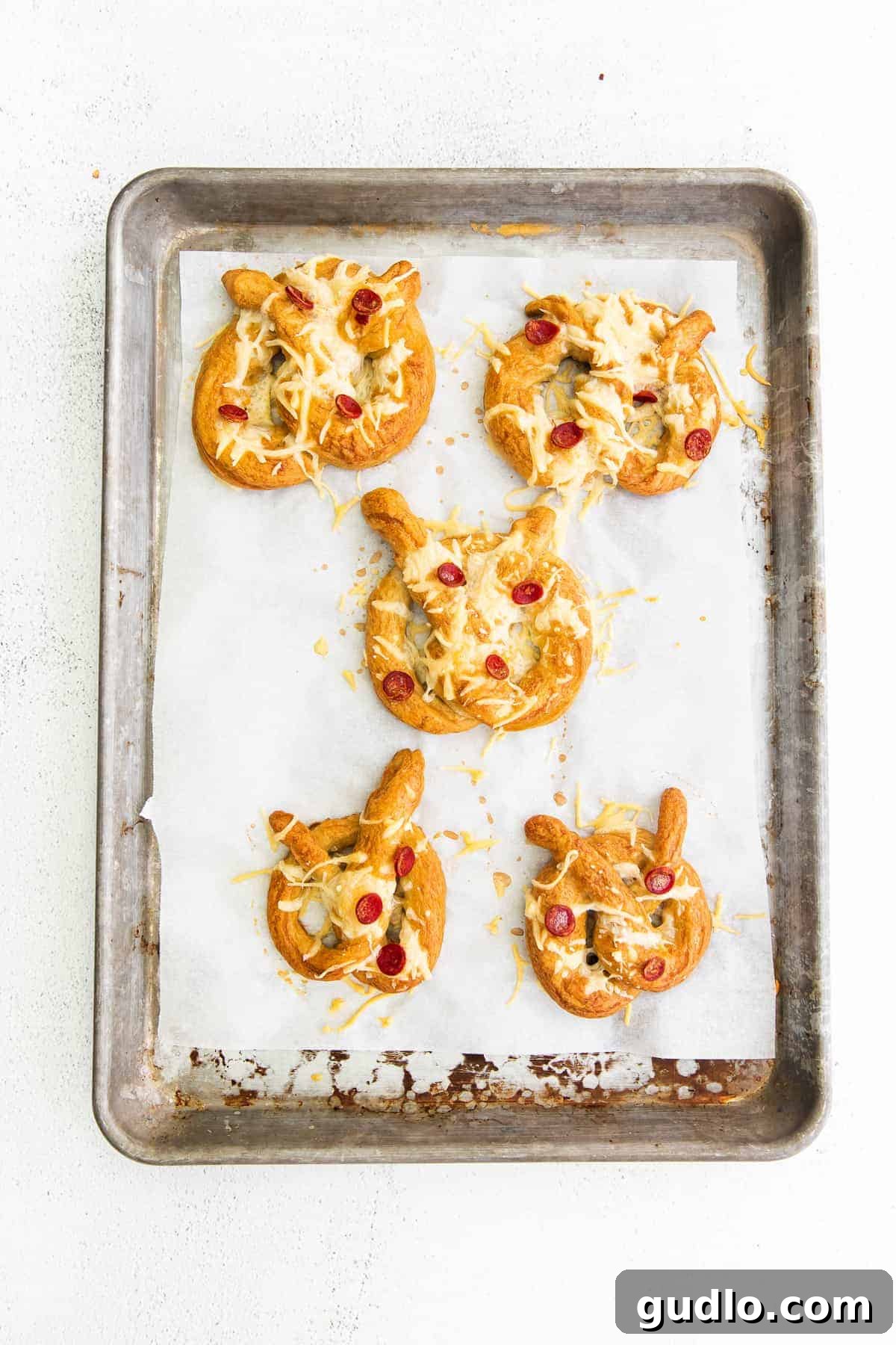 These pizza soft pretzels are such a fun snack or appetizer to make that the whole family will enjoy. Top them with your favorite pizza toppings! Five perfectly baked pizza soft pretzels cooling on a baking sheet, showcasing melted cheese, crispy pepperoni, and golden crusts.