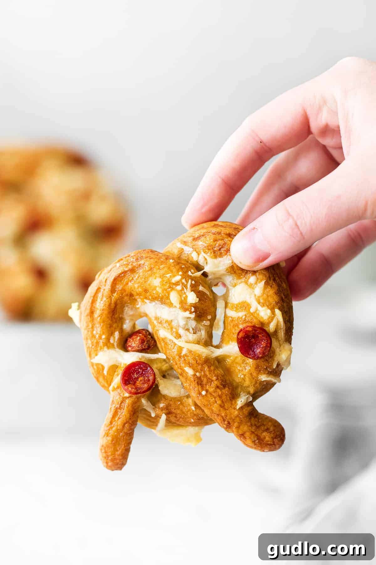 These pizza soft pretzels are such a fun snack or appetizer to make that the whole family will enjoy. Top them with your favorite pizza toppings! A hand holding a perfectly golden-brown pizza soft pretzel, showcasing the melted cheese and pepperoni toppings, ready to be eaten.