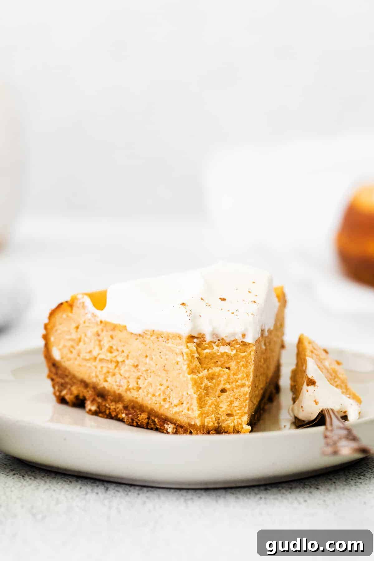 Chai Pumpkin Cheesecake: The Perfect Fall Treat A perfectly sliced piece of Chai Pumpkin Cheesecake on a white plate, garnished with a dollop of whipped cream and a sprinkle of chai spice, invitingly ready to be enjoyed.