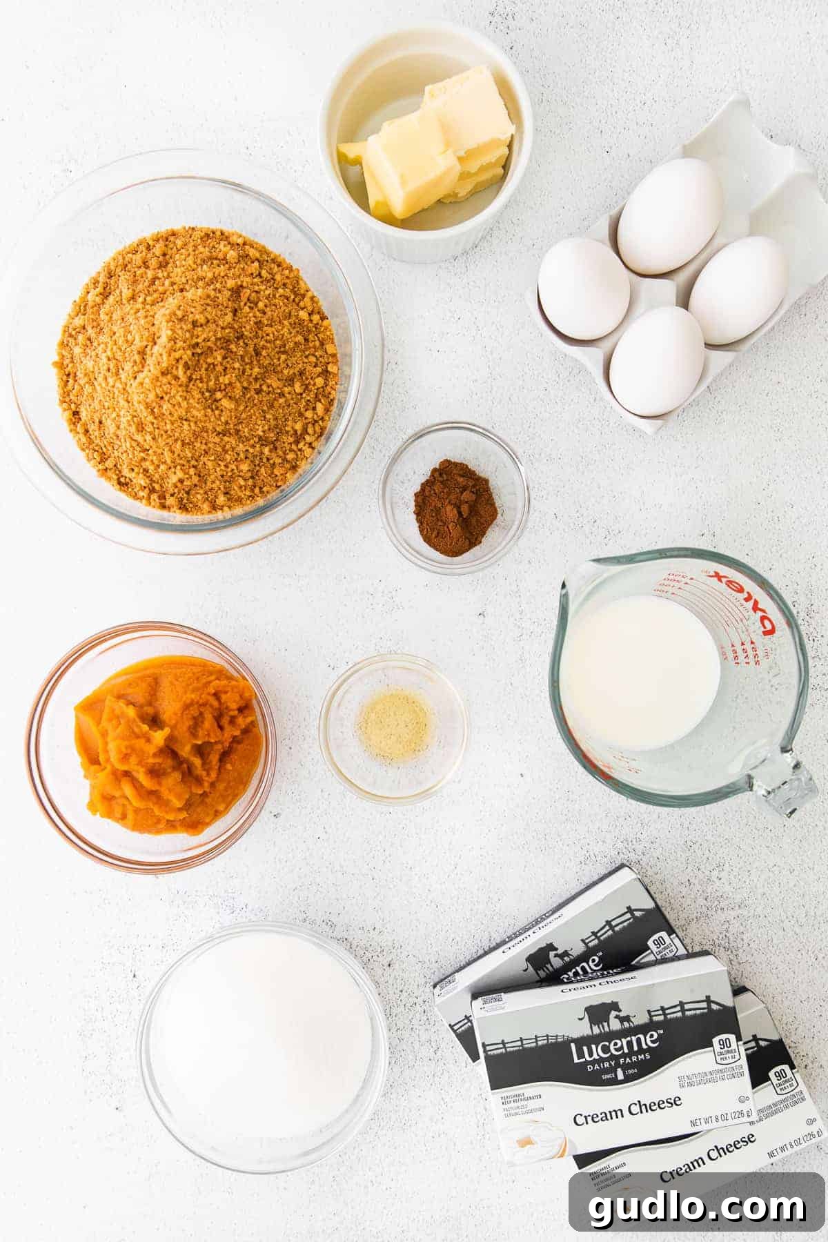 Chai Pumpkin Cheesecake Ingredients Ready Essential ingredients for Chai Pumpkin Cheesecake, including cream cheese, pumpkin puree, chai spices, and ginger snaps, neatly arranged and ready for preparation on a rustic wooden surface.