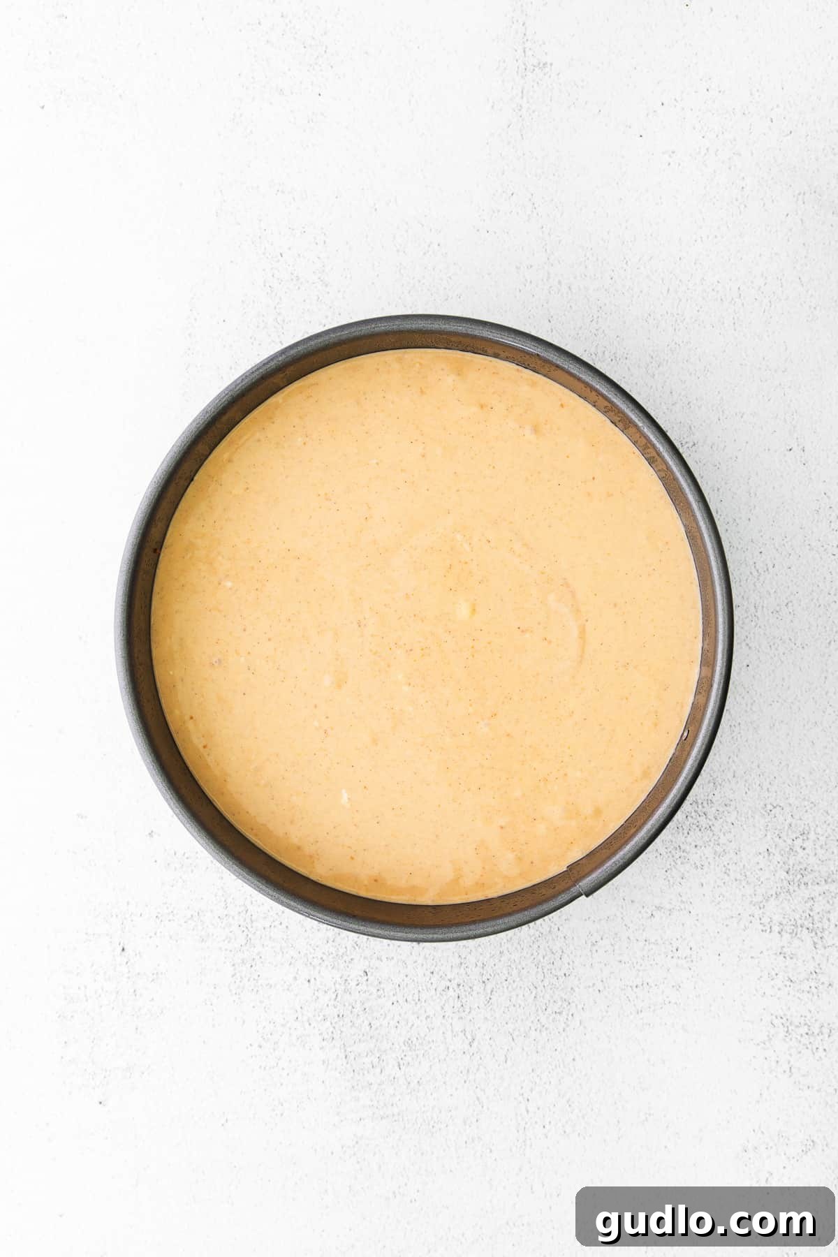 Chai Pumpkin Cheesecake Filling Ready for Baking Smooth and creamy pumpkin chai cheesecake filling in a springform pan, perfectly leveled and ready to be baked in the oven, with a warm, inviting hue.