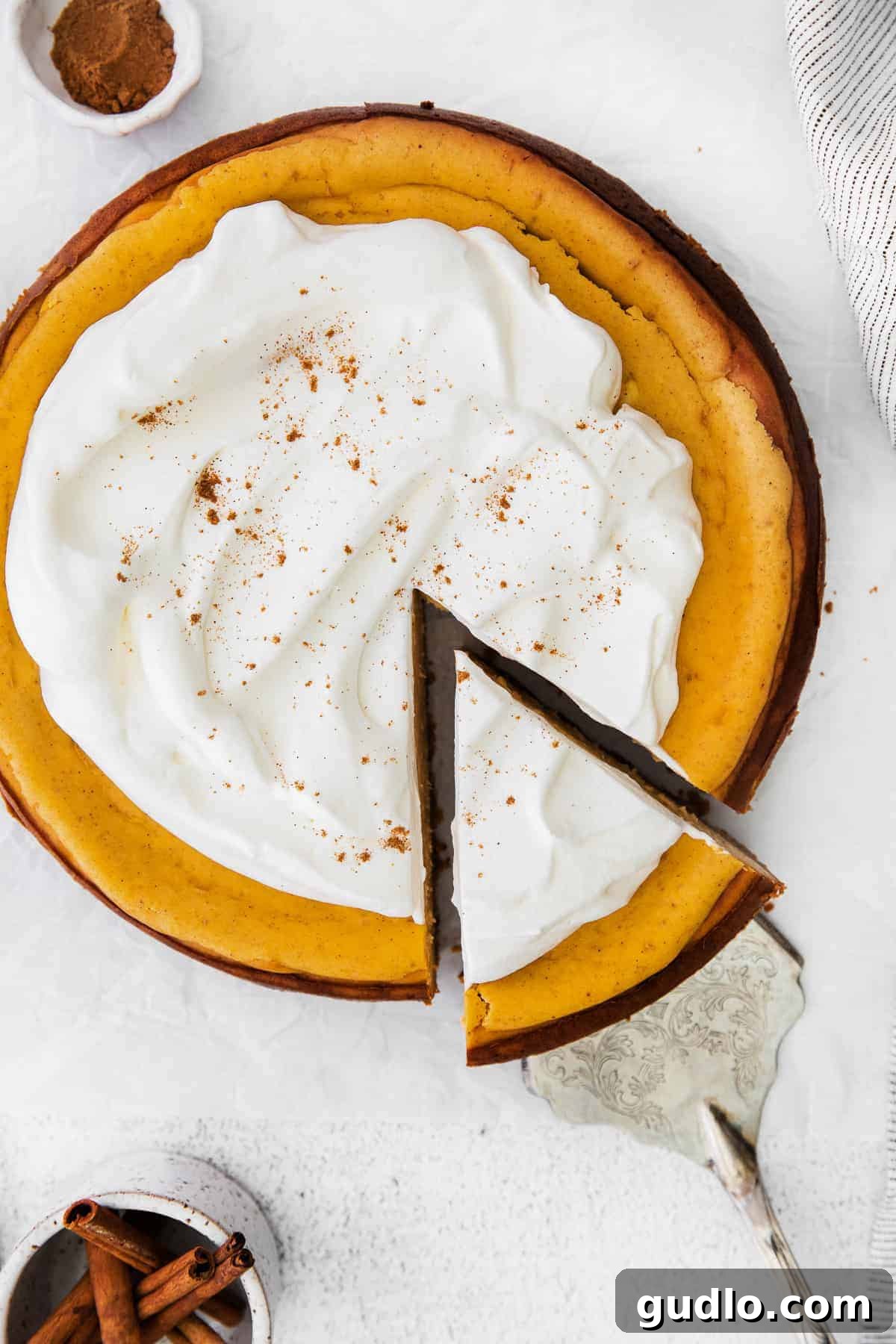 Chai Pumpkin Cheesecake with Whipped Cream Topping A beautiful slice of Chai Pumpkin Cheesecake artfully topped with a swirl of fresh whipped cream and a delicate dusting of chai spice, presented on a minimalist white plate.
