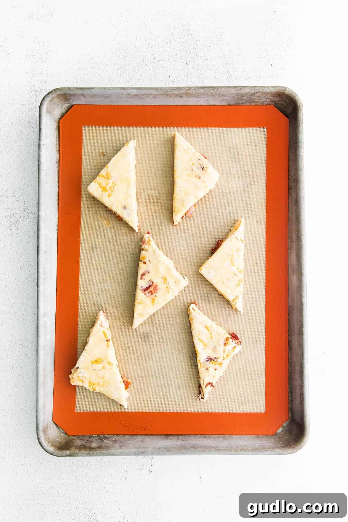 Unbaked bacon and cheddar scones, perfectly shaped and arranged on a parchment-lined baking sheet, ready for the oven.