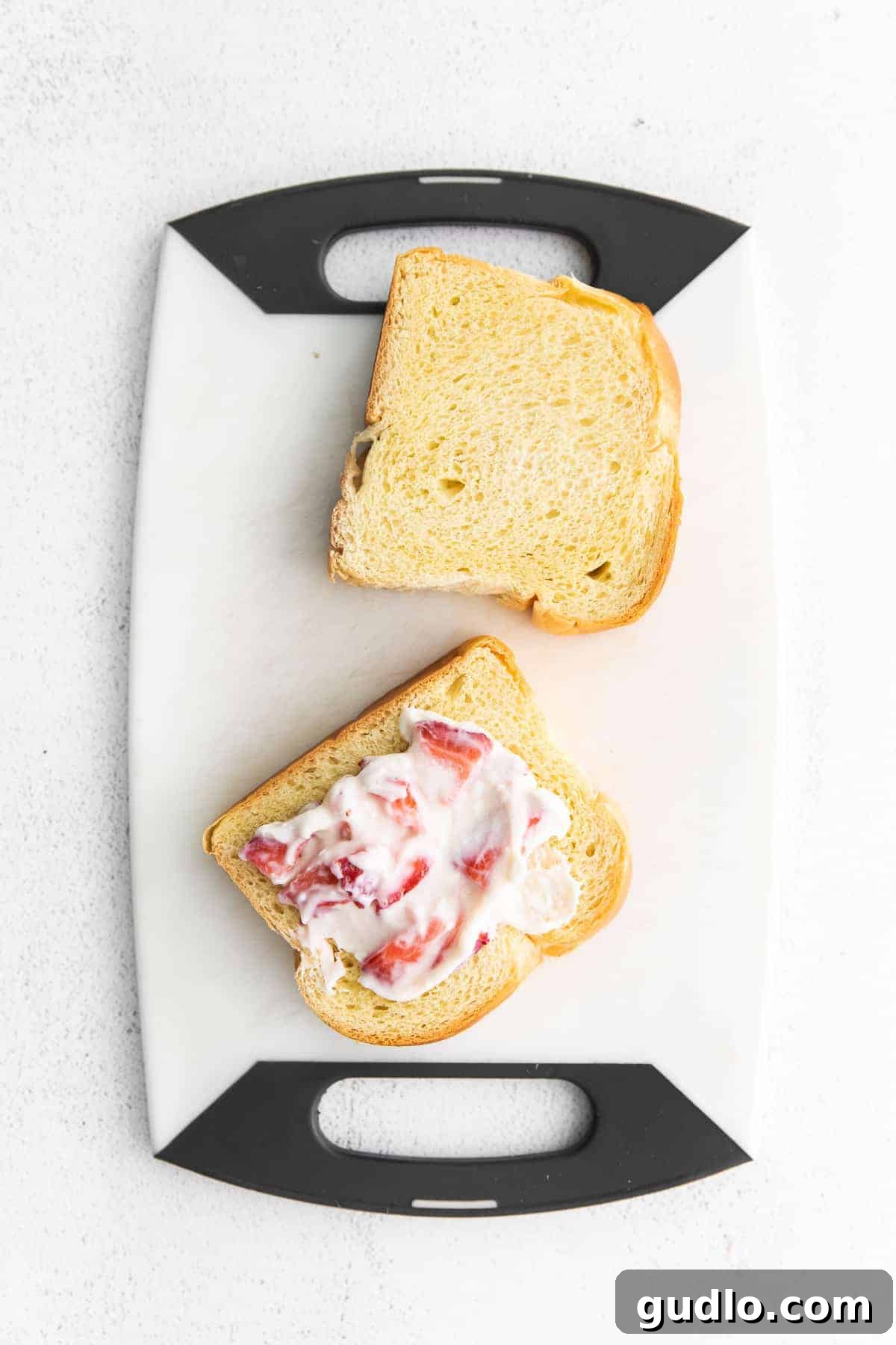 Two slices of brioche bread being prepared with a strawberry cream cheese mixture for stuffed French toast.