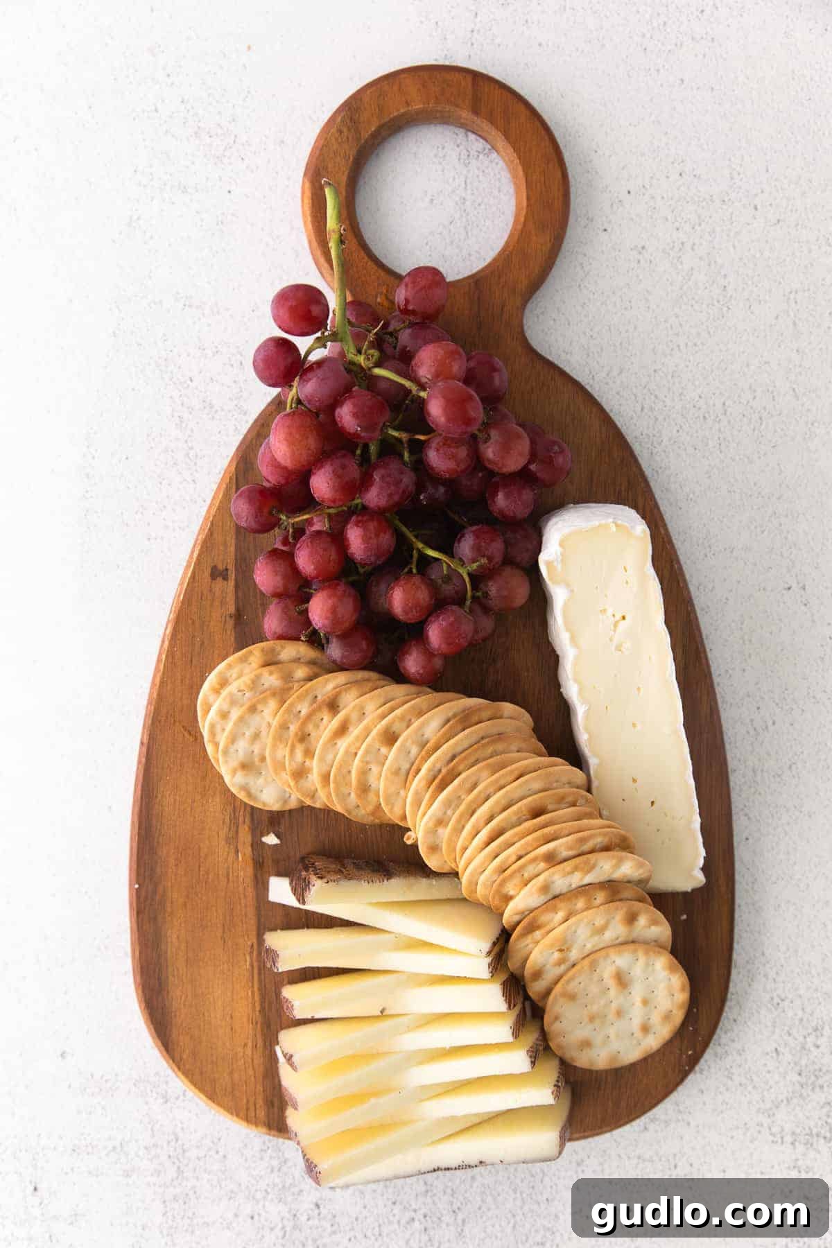 The initial layout of large ingredients like grapes, brie, and manchego on a chocolate and cheese board.