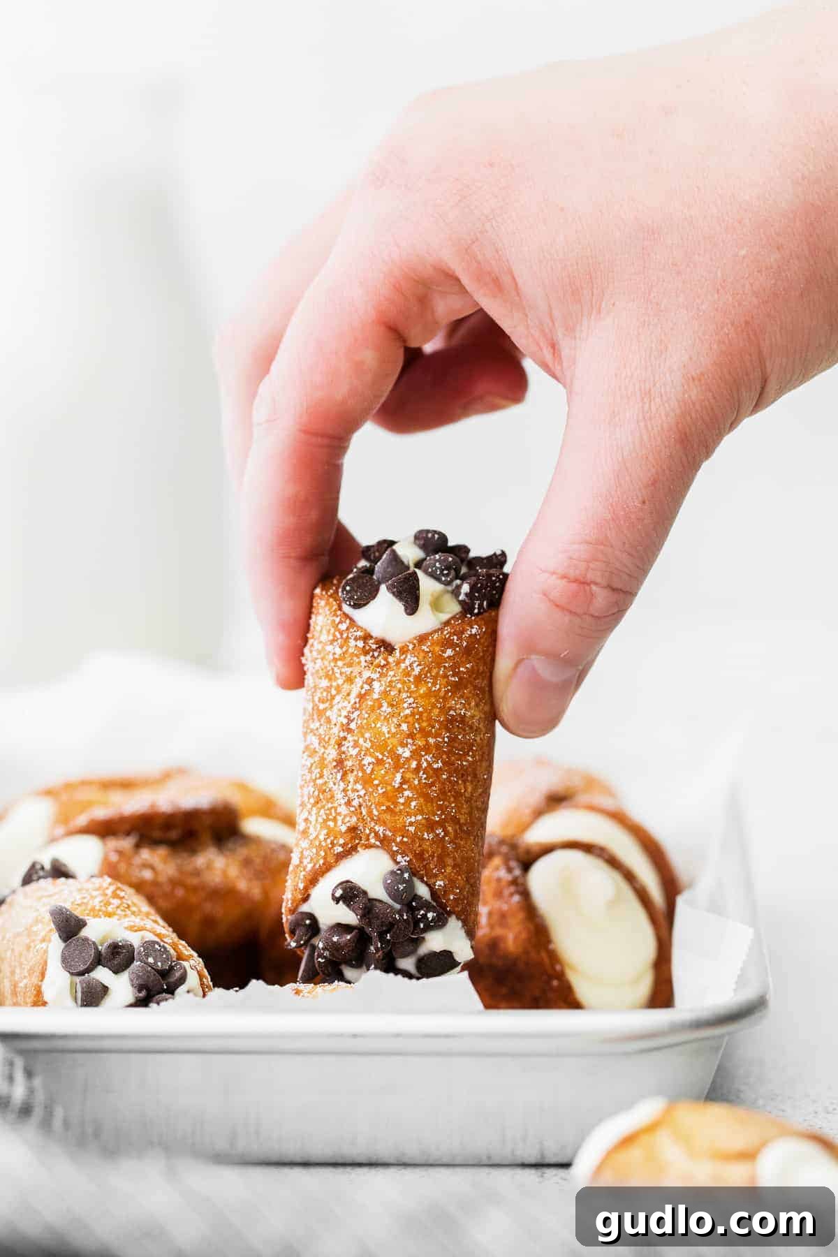 Authentic Italian Cannolis 2 A hand holding a perfectly golden-brown cannoli, showcasing its crispy shell and creamy filling.