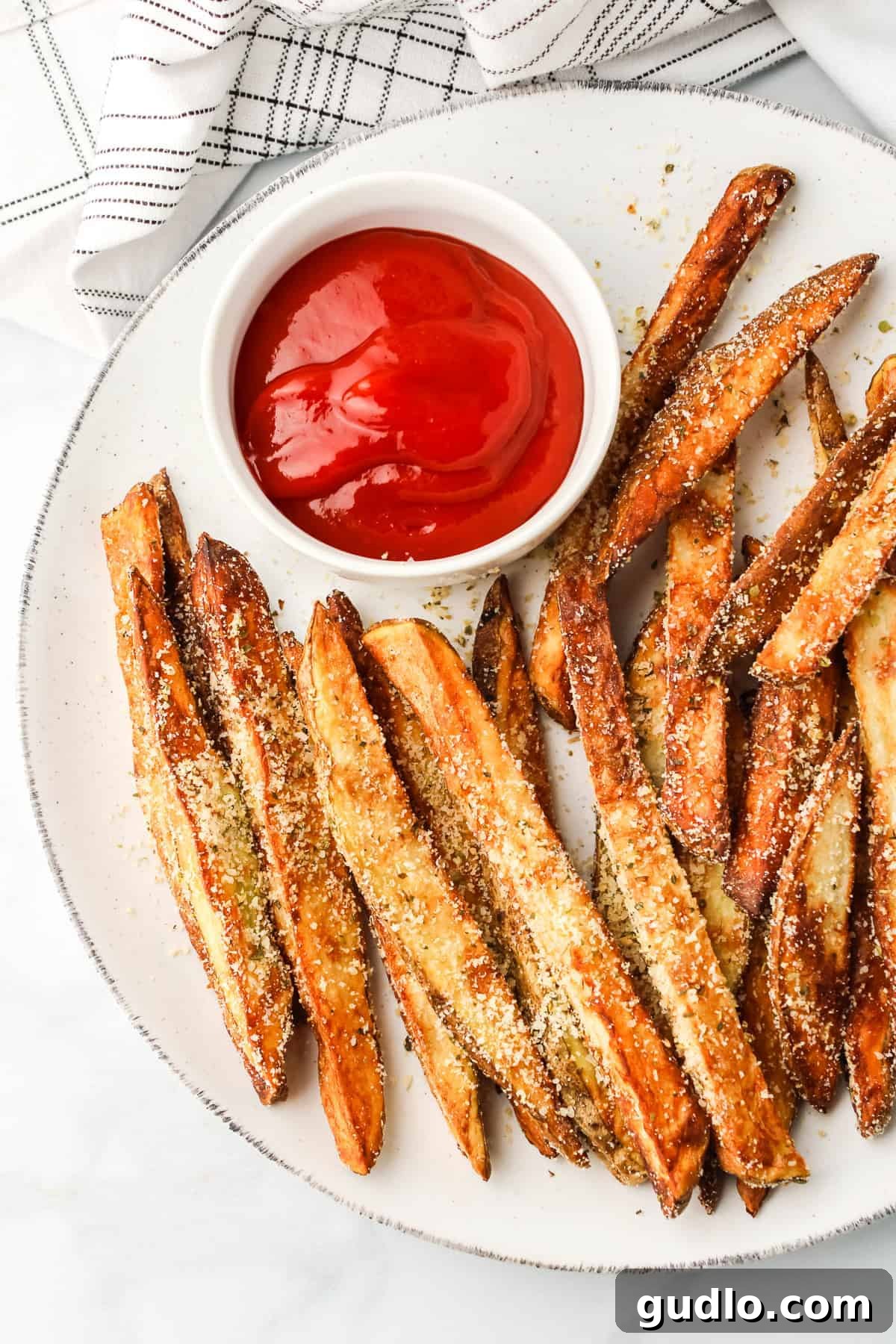 Crispy garlic parmesan fries served on a plate with a side of ketchup.