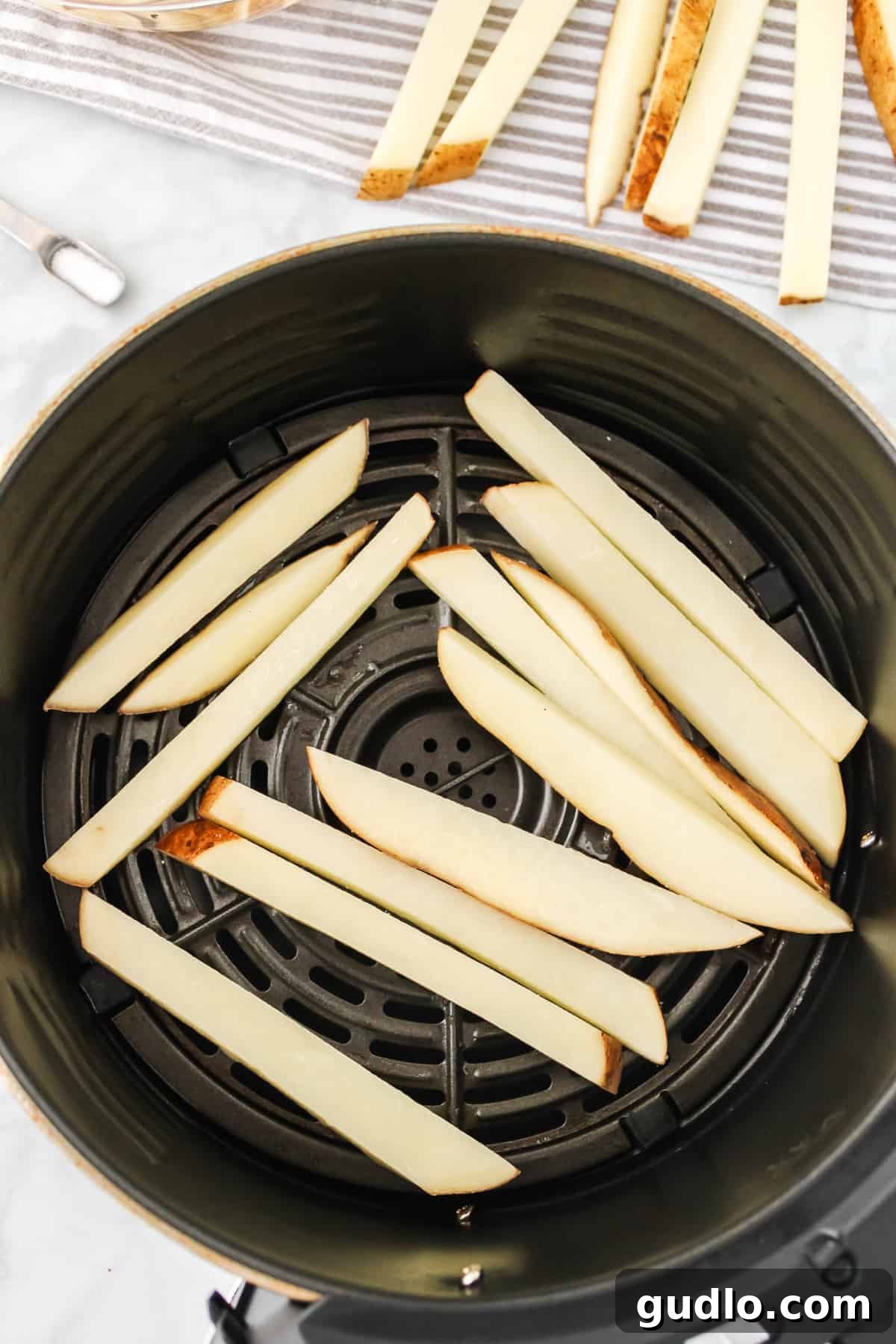 Salted and oiled potato fries arranged in a single layer inside an air fryer basket.